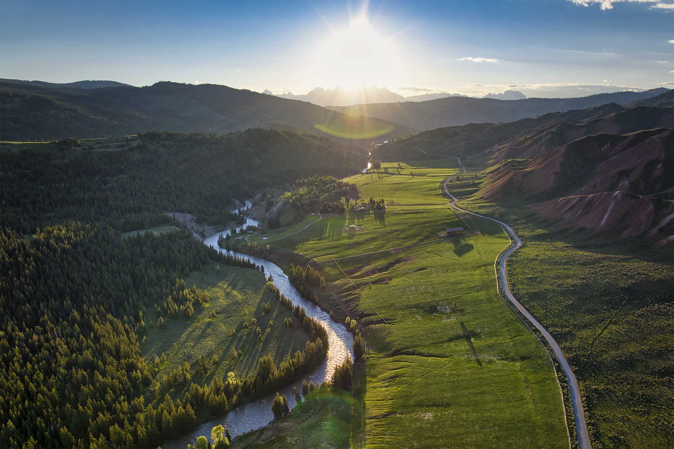 The Triple Bar M Ranch, Wyoming — aerial view of green valleys and mountain peaks at sunset